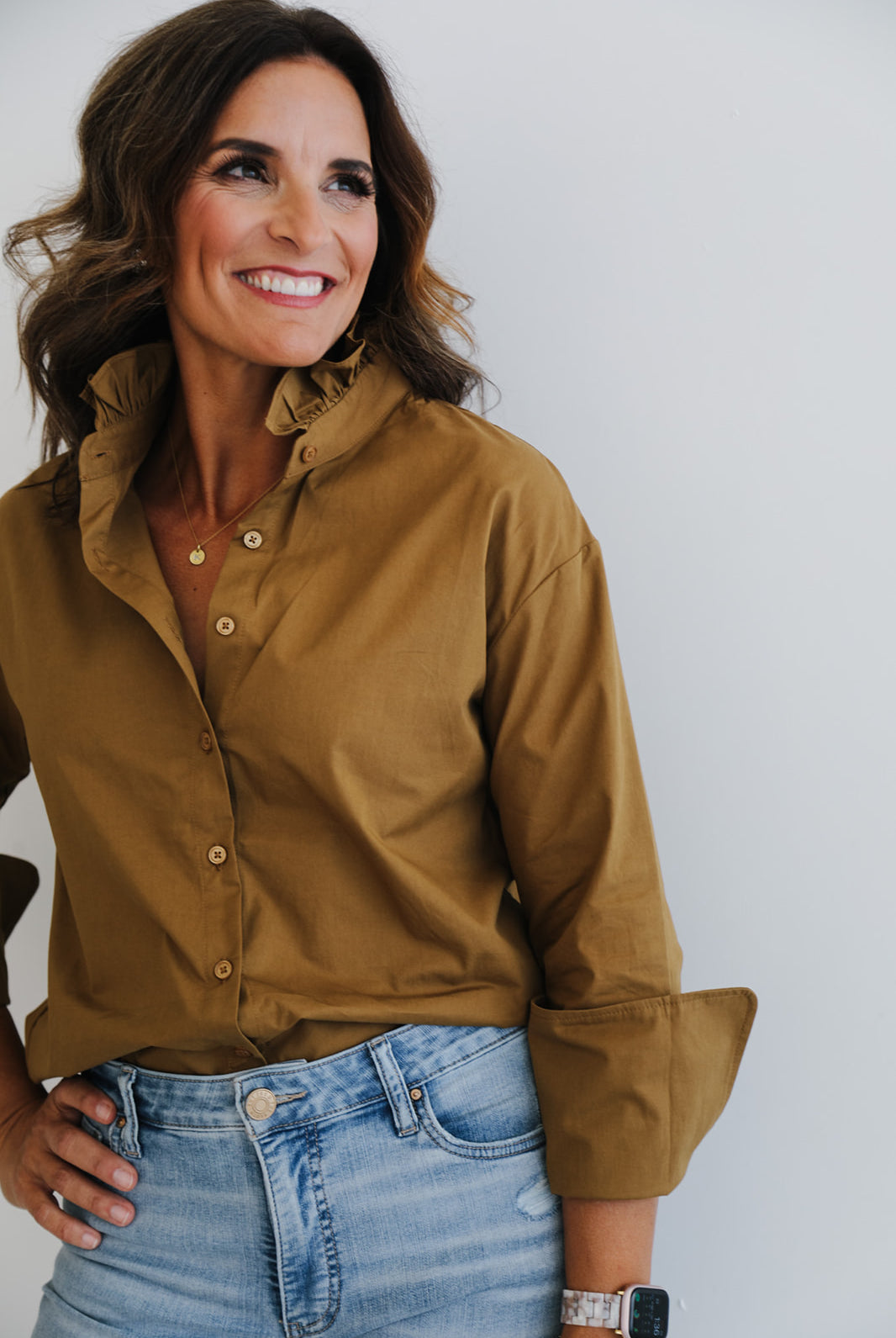 Woman wearing a brown button-up shirt and blue jeans against a plain background
