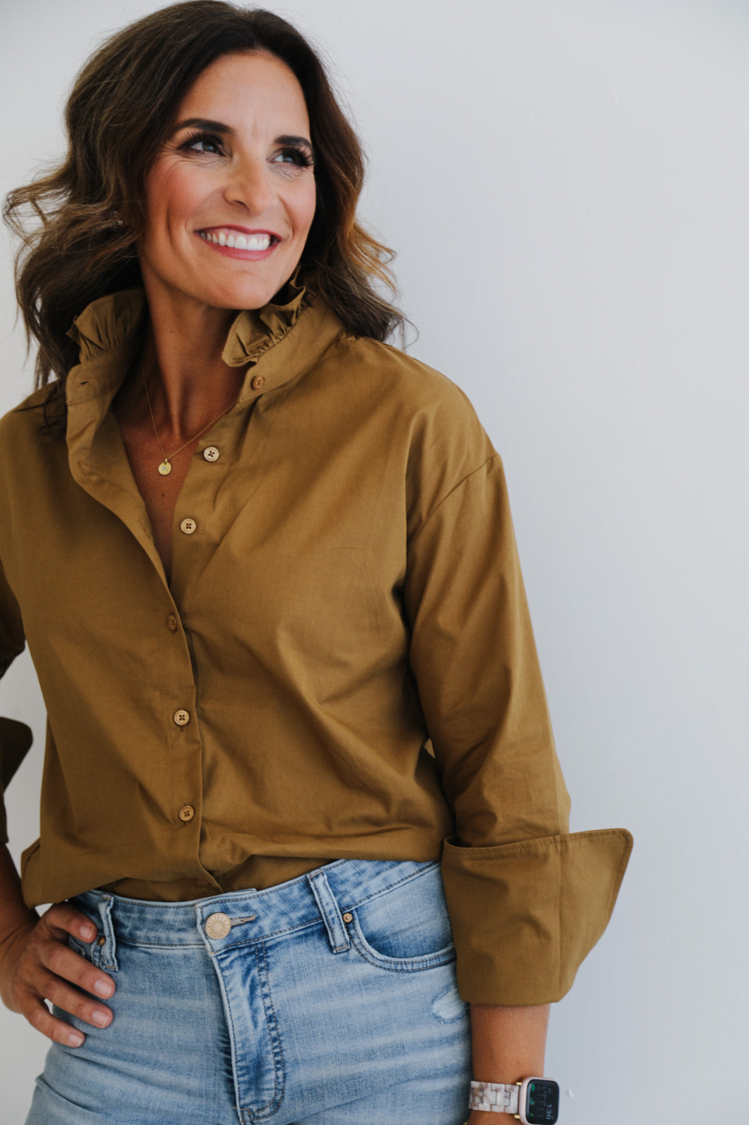 Woman wearing a brown button-up shirt and blue jeans against a plain background