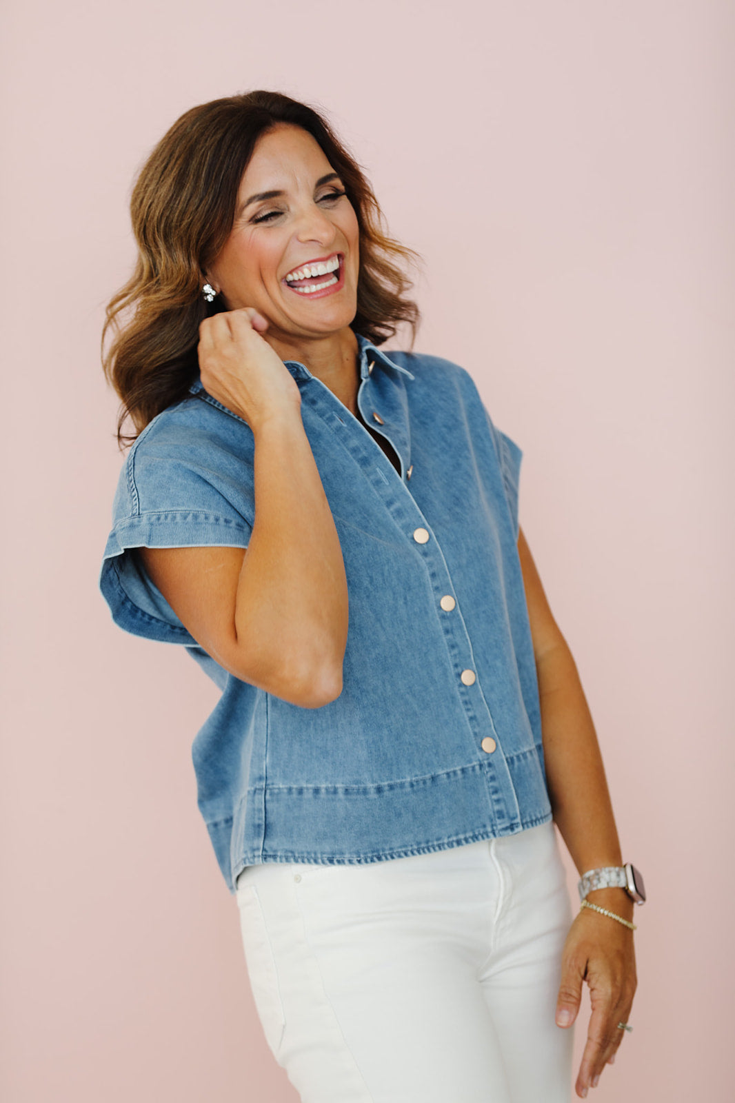 Woman wearing a denim vest against a pink background