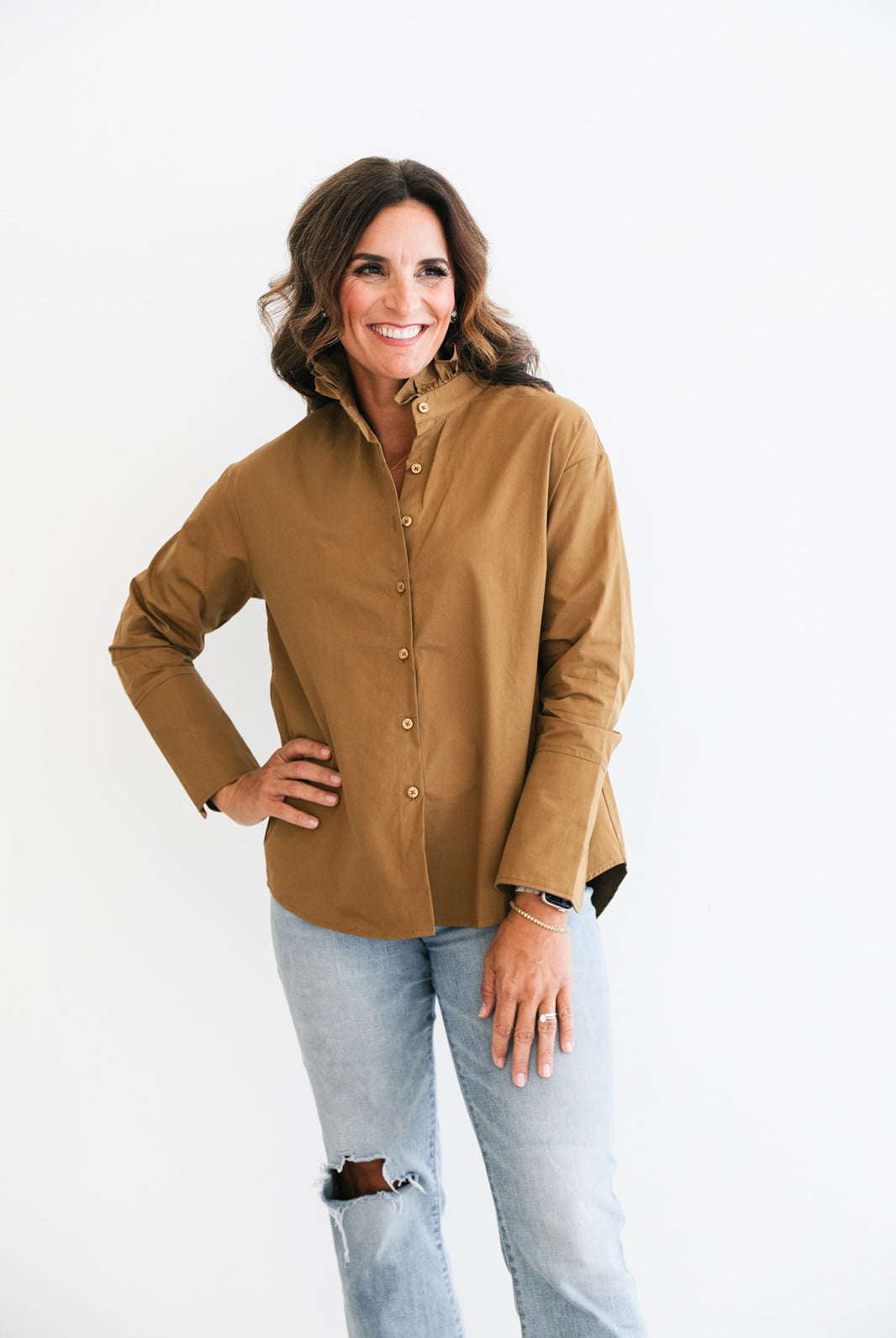 Woman wearing a brown button-up shirt and light blue jeans on a white background