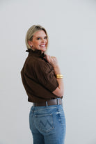 Woman wearing a brown blouse and blue jeans against a plain background