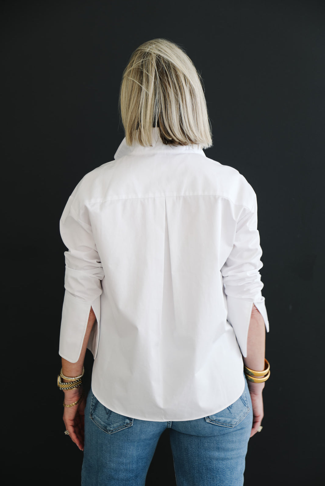 Woman wearing a white shirt and blue jeans against a black background