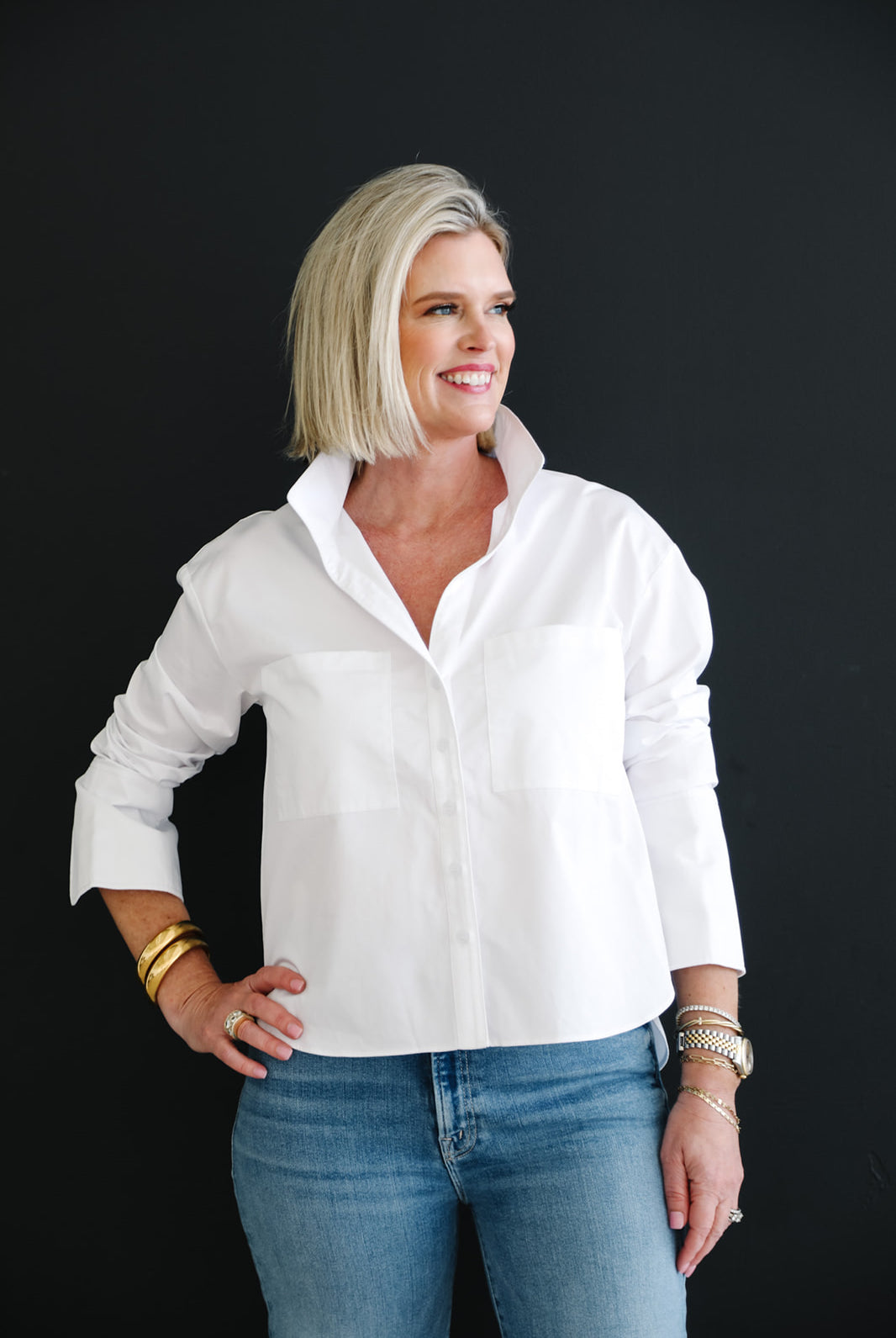 Woman wearing a white shirt and blue jeans against a black background