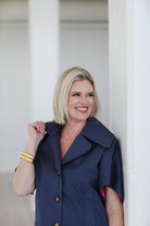 Woman wearing a navy blue coat standing against a white wall.