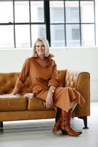 Woman in a brown outfit sitting on a leather couch with large windows in the background