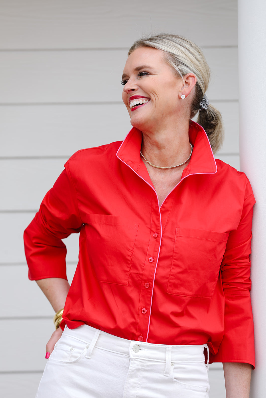 Woman standing in front of a white wall wearing a red button up shirt with contrast pink piping.