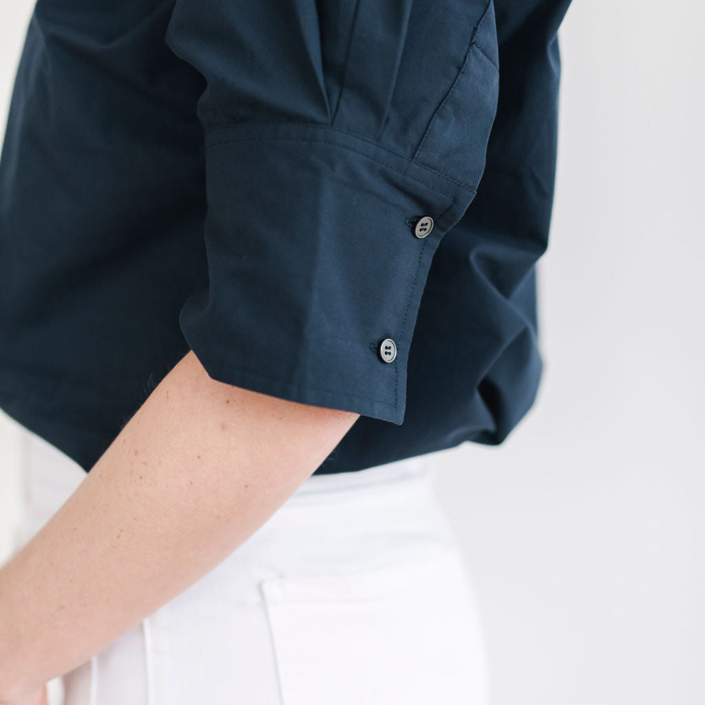 Navy blue cotton pullover style shirt with a stand up collar, a longer short sleeve with button details.