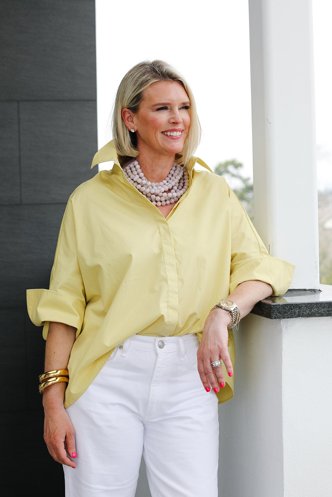 Woman wearing a yellow shirt and white pants standing against a neutral background