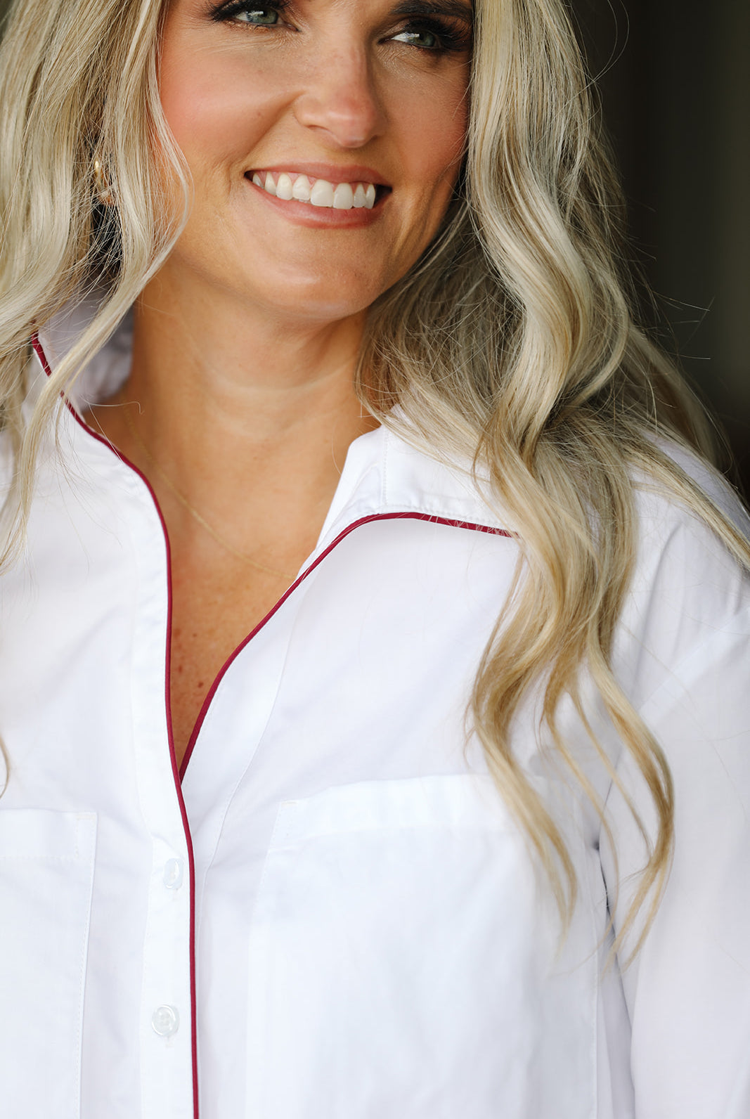 Woman wearing a white shirt with maroon trim, smiling.