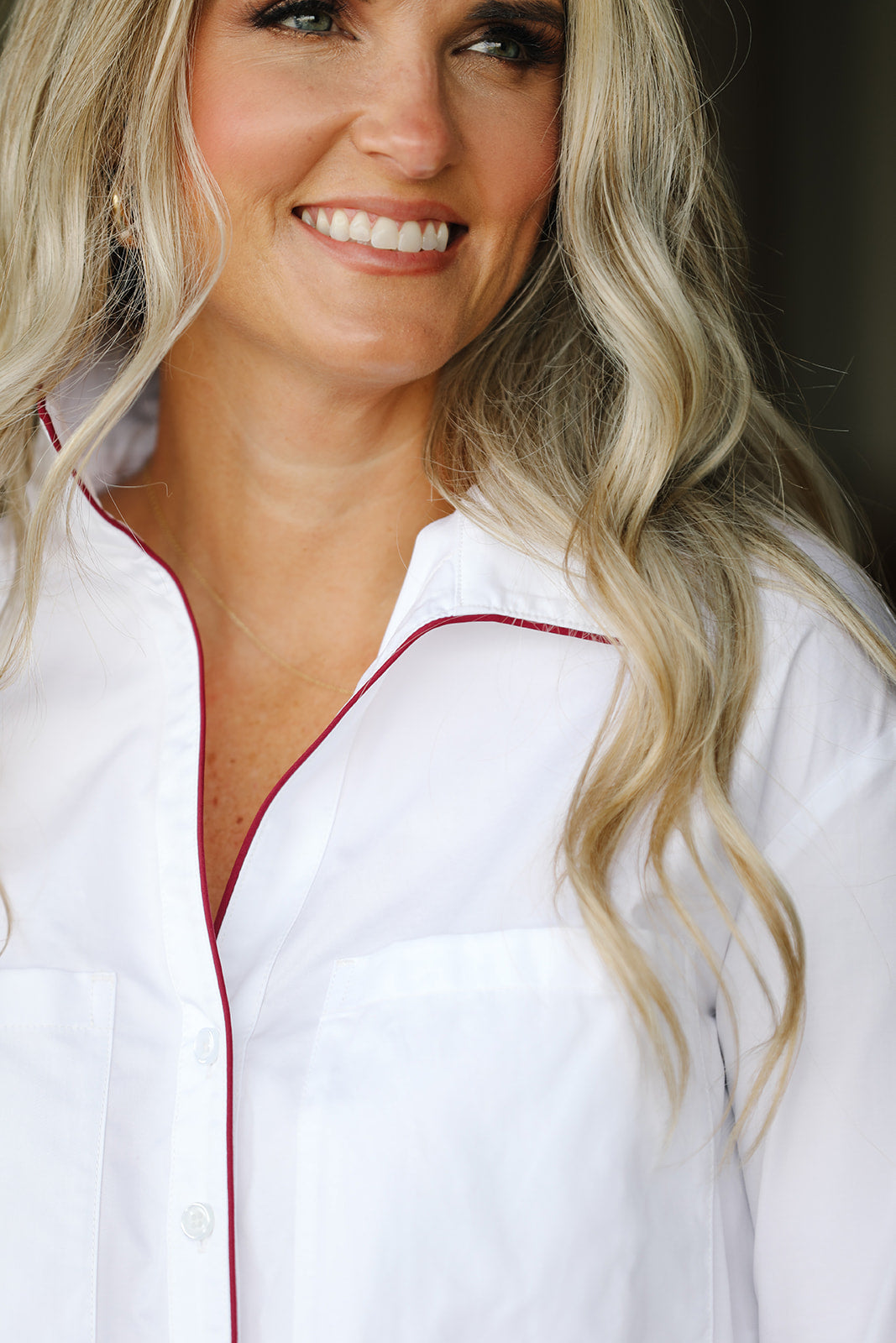 Woman wearing a white shirt with maroon trim, smiling.