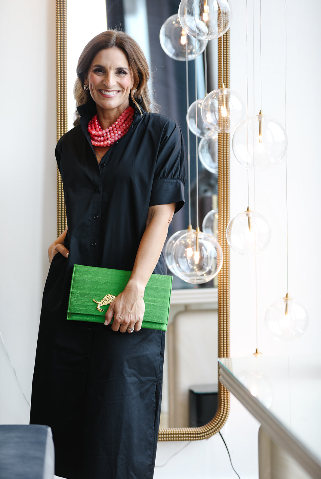 Woman in a black dress holding a green clutch in an indoor setting with modern decor.