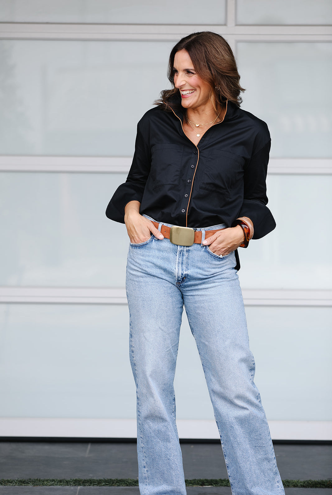 Woman wearing a black shirt and light blue jeans against a gray wall.