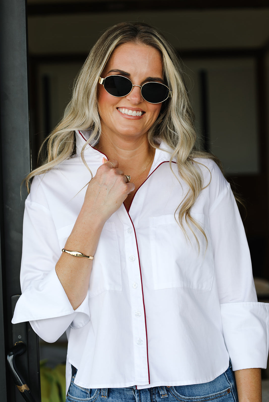 Woman wearing a white blouse with maroon trim and sunglasses, standing indoors.