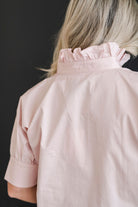 A crisp and classic shirt in a blush pink color with a ruffle collar.