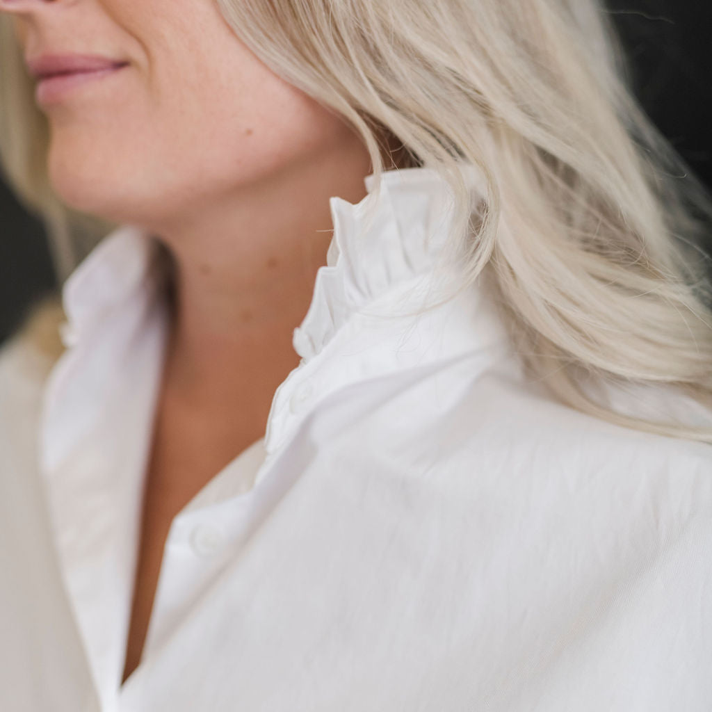 A white long sleeve button up shirt with a stand up ruffle collar and oversized cuffs.