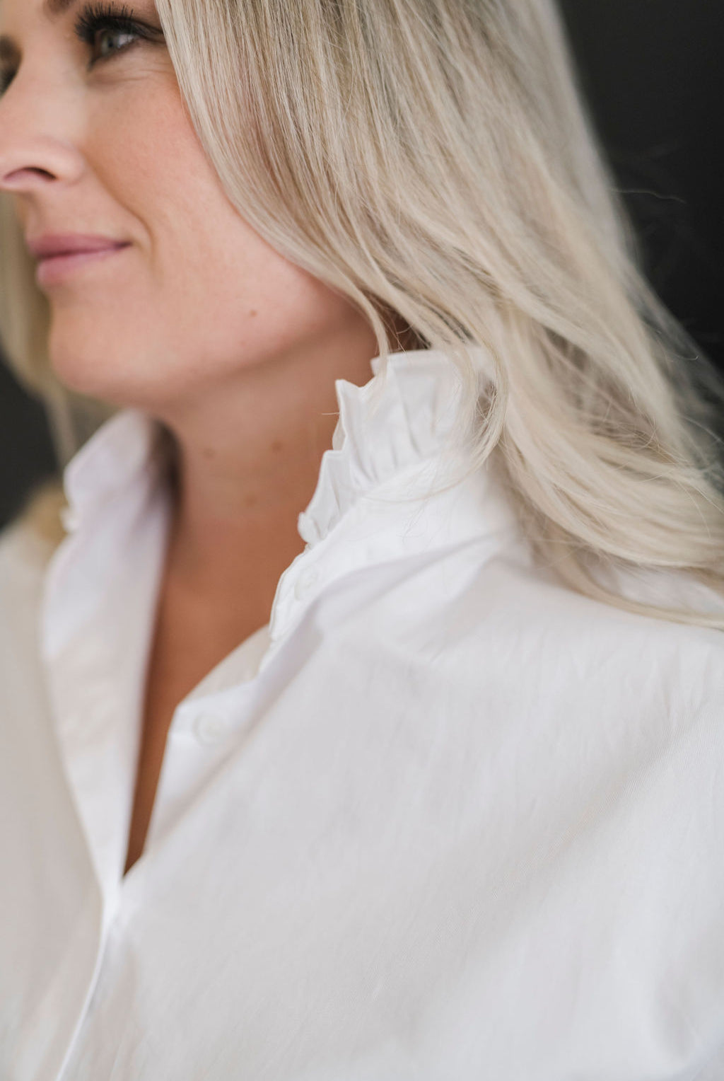 A white long sleeve button up shirt with a stand up ruffle collar and oversized cuffs.