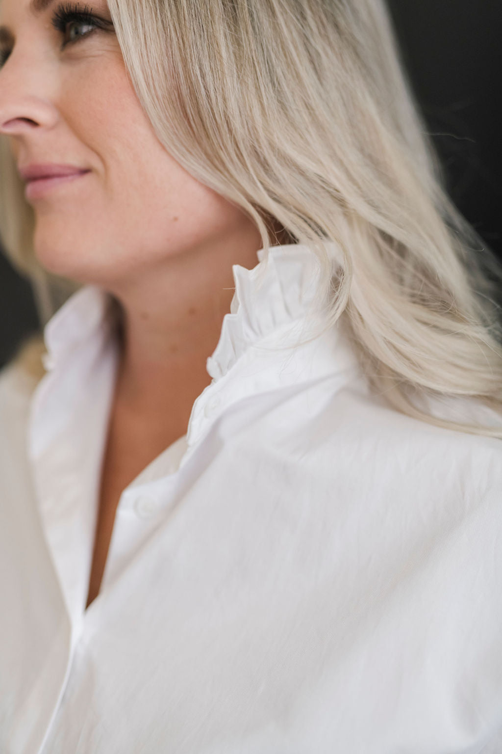 A white long sleeve button up shirt with a stand up ruffle collar and oversized cuffs.