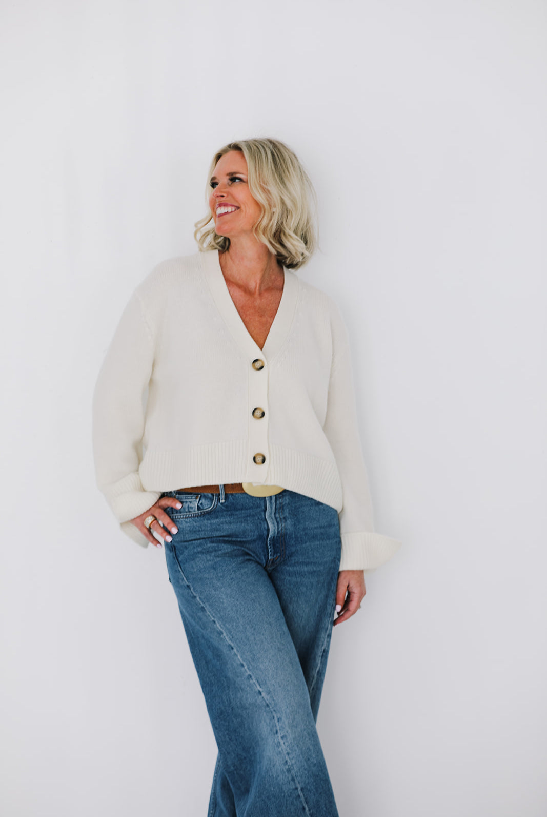 Woman wearing a cream cardigan and blue jeans against a white background
