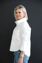 Woman wearing a white shirt and blue jeans against a black background