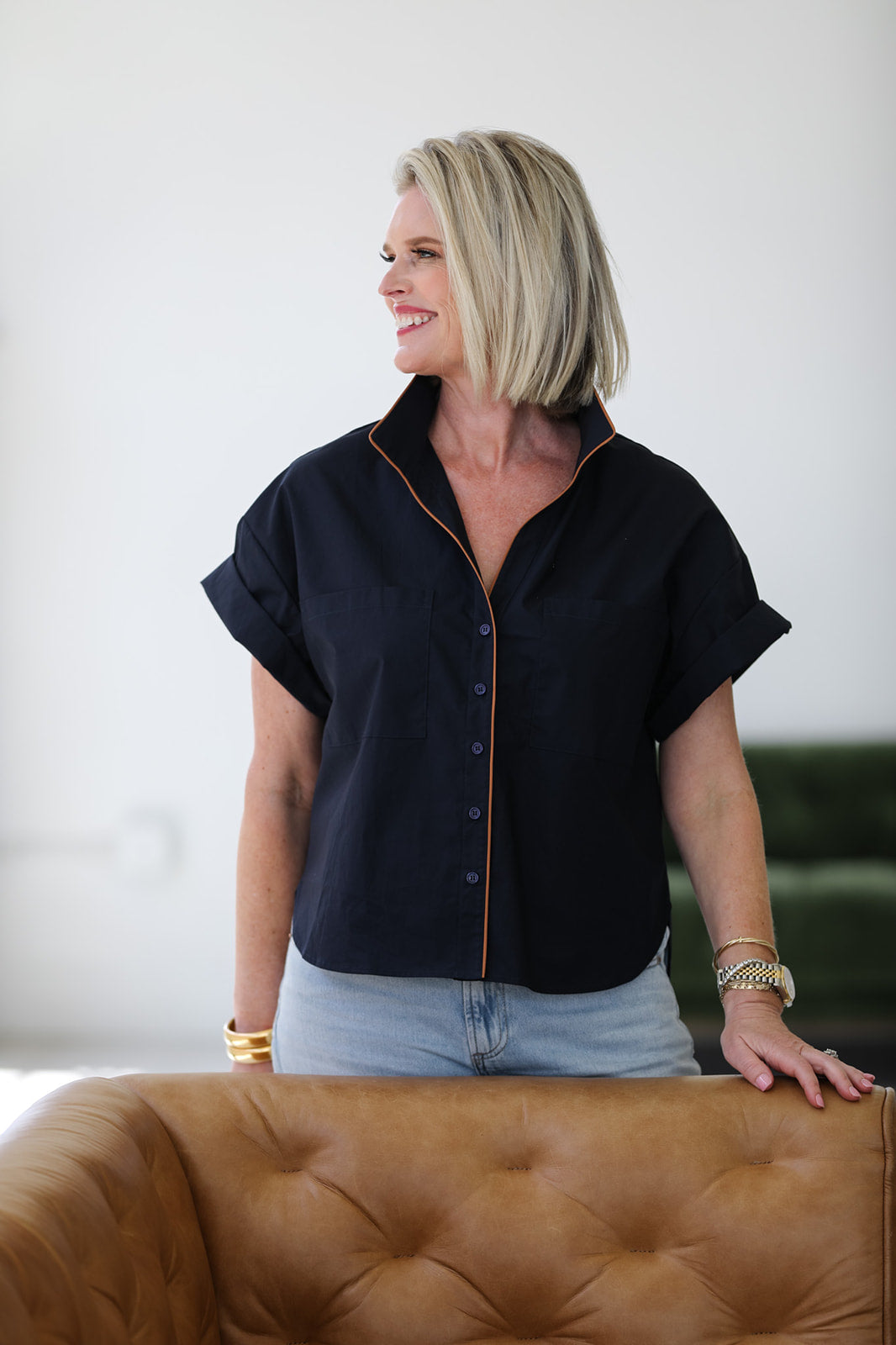 Woman wearing a dark navy short-sleeve shirt with brown piping in a casual setting.