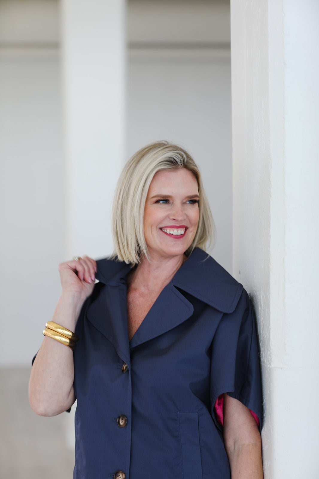 Woman wearing a navy blue coat standing against a white wall.