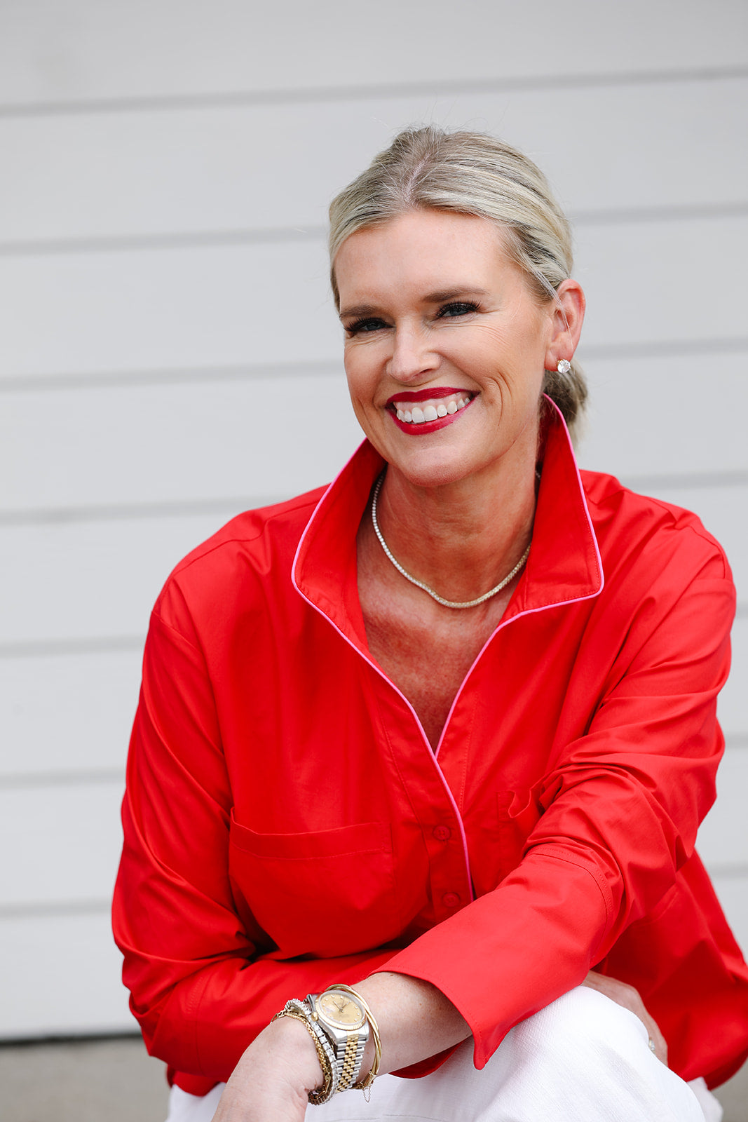 Woman standing in front of a white wall wearing a red button up shirt with contrast pink piping.