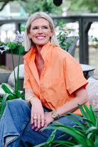 Woman wearing an orange shirt and blue jeans sitting among plants.