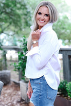 Woman wearing a white blouse and blue shorts outdoors with greenery in the background