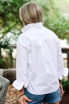 Person wearing a white shirt and denim shorts standing outdoors with greenery in the background