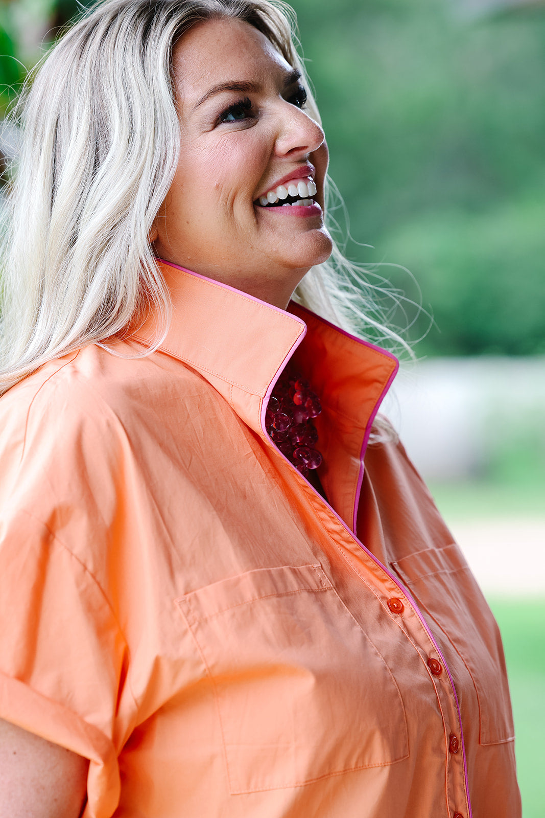 Woman wearing an orange shirt with a blurred green background