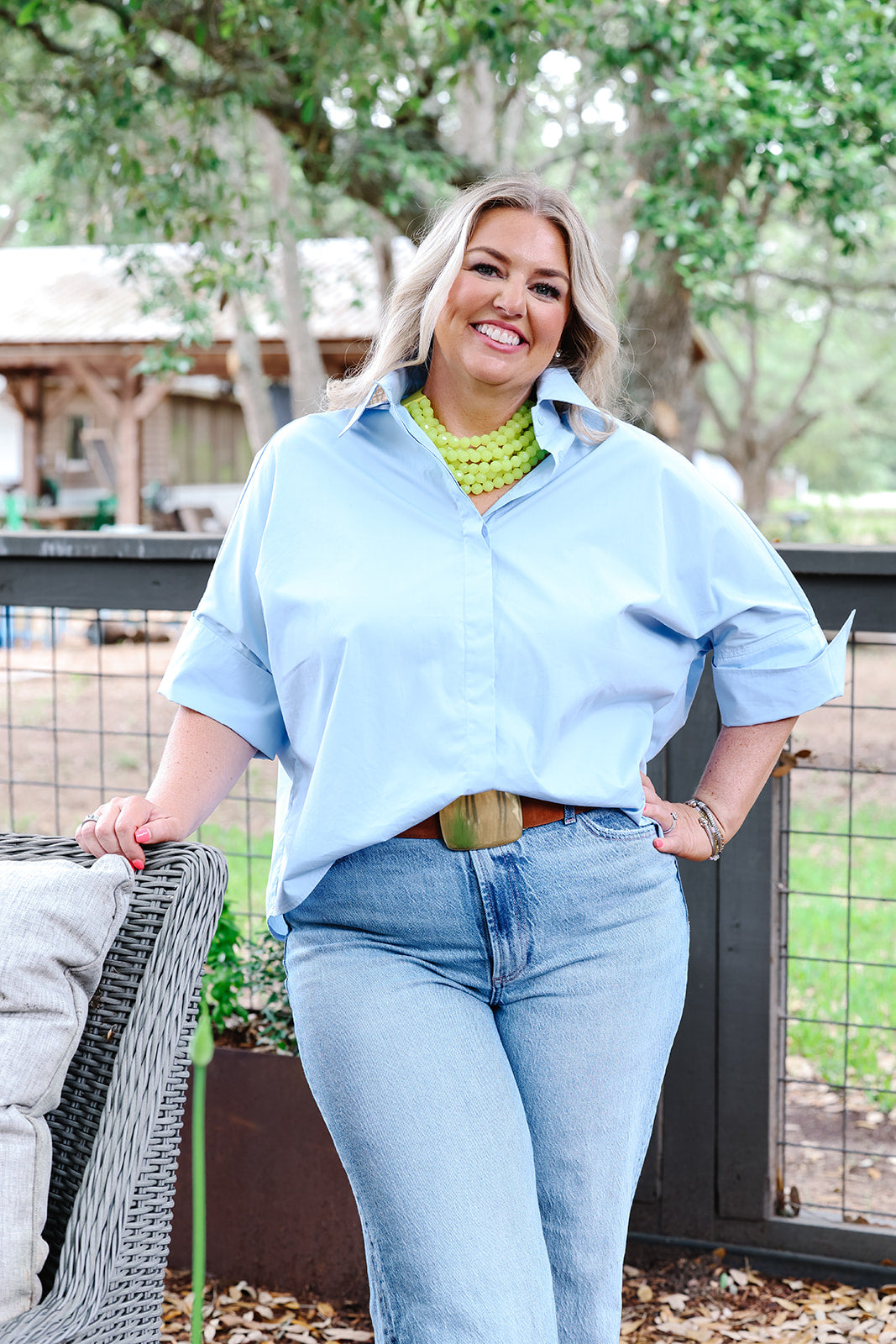 Woman wearing a light blue shirt and jeans standing outdoors with trees in the background
