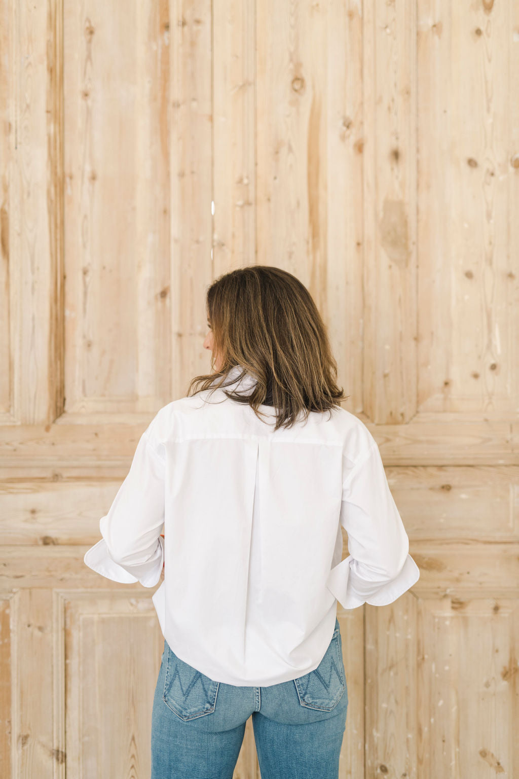 Crisp white women's button down shirt showing the back with a center pleat.