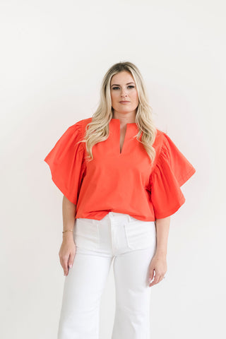 Bright orange statement top with dramatic sleeves, paired with white jeans.