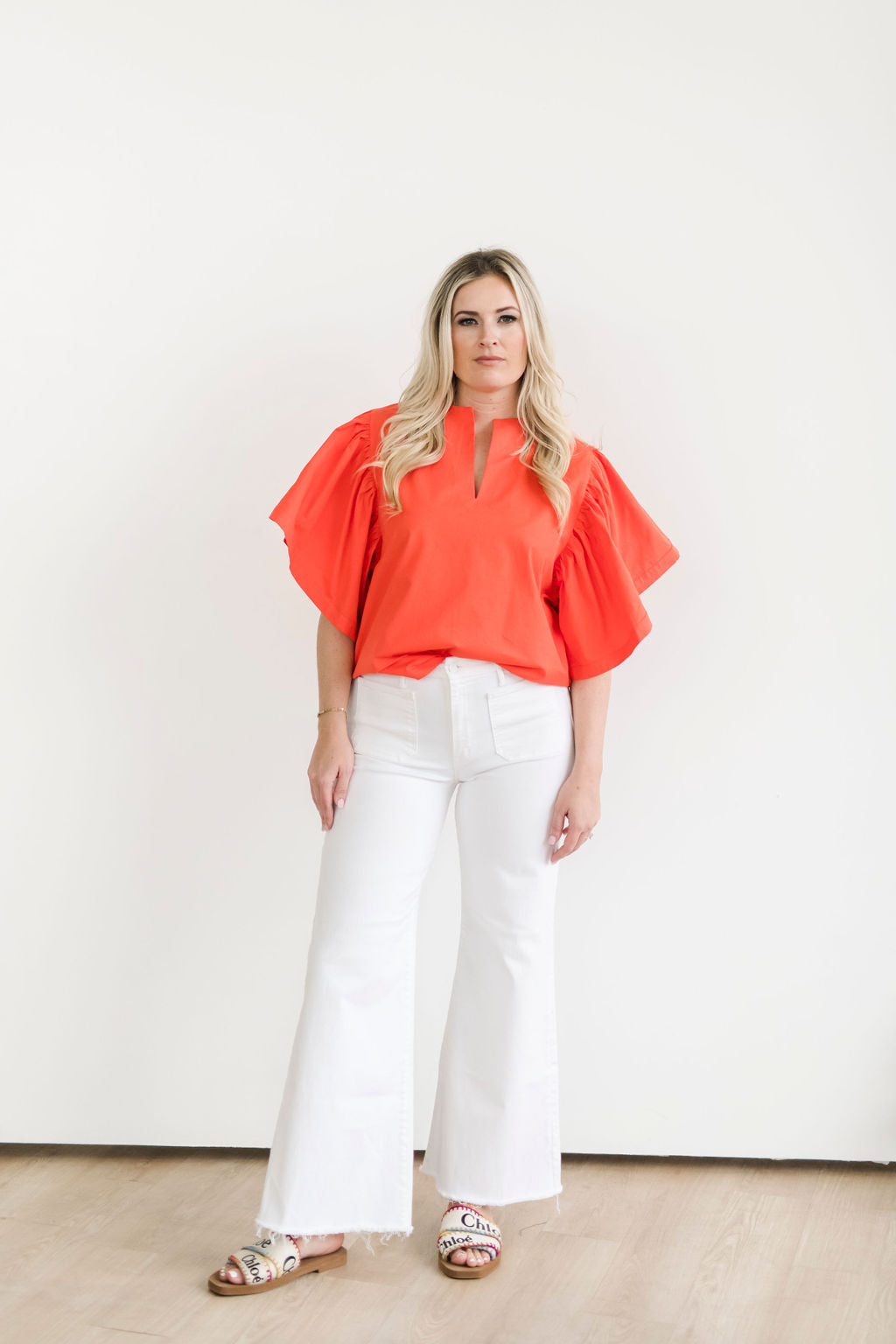 Bright orange statement top with dramatic sleeves, paired with white jeans.