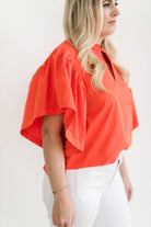 Bright orange statement top with dramatic sleeves, paired with white jeans.