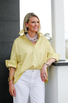 Woman wearing a yellow shirt and white pants standing against a neutral background