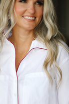 Woman wearing a white shirt with maroon trim, smiling.
