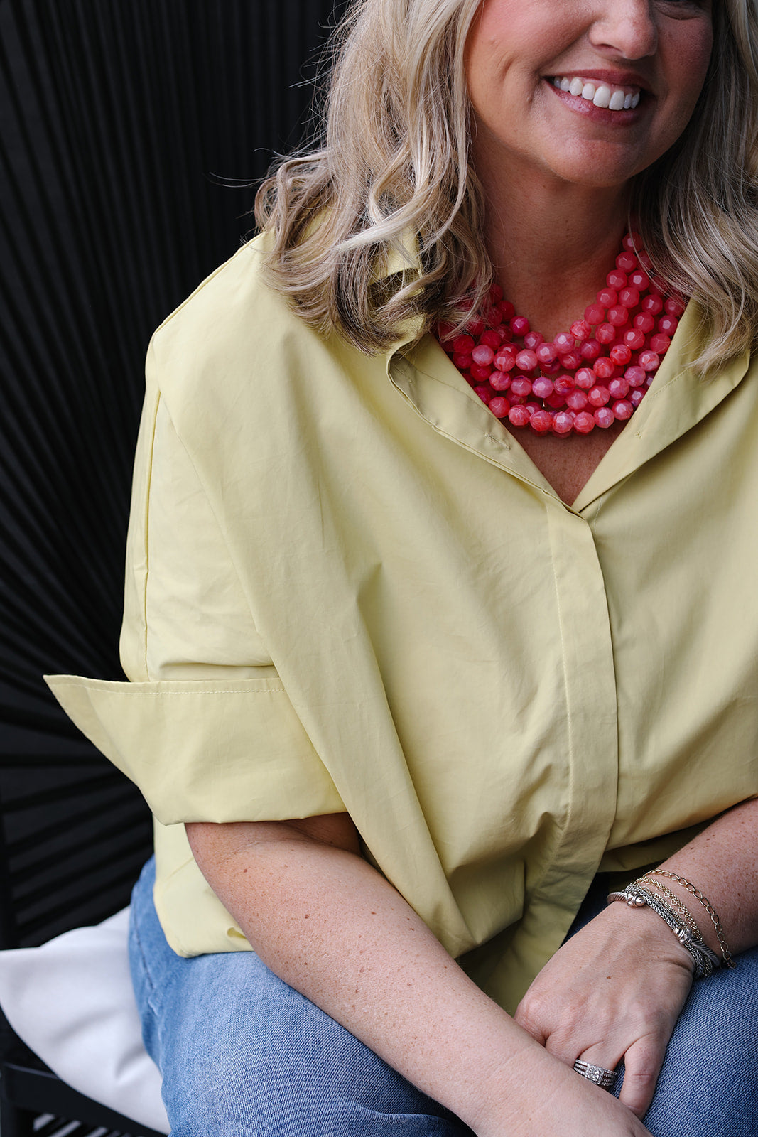Woman wearing a yellow shirt and pink necklace with a blurred background