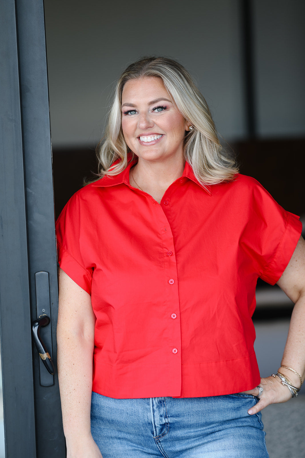 Woman wearing a red shirt and blue jeans standing in front of a dark background