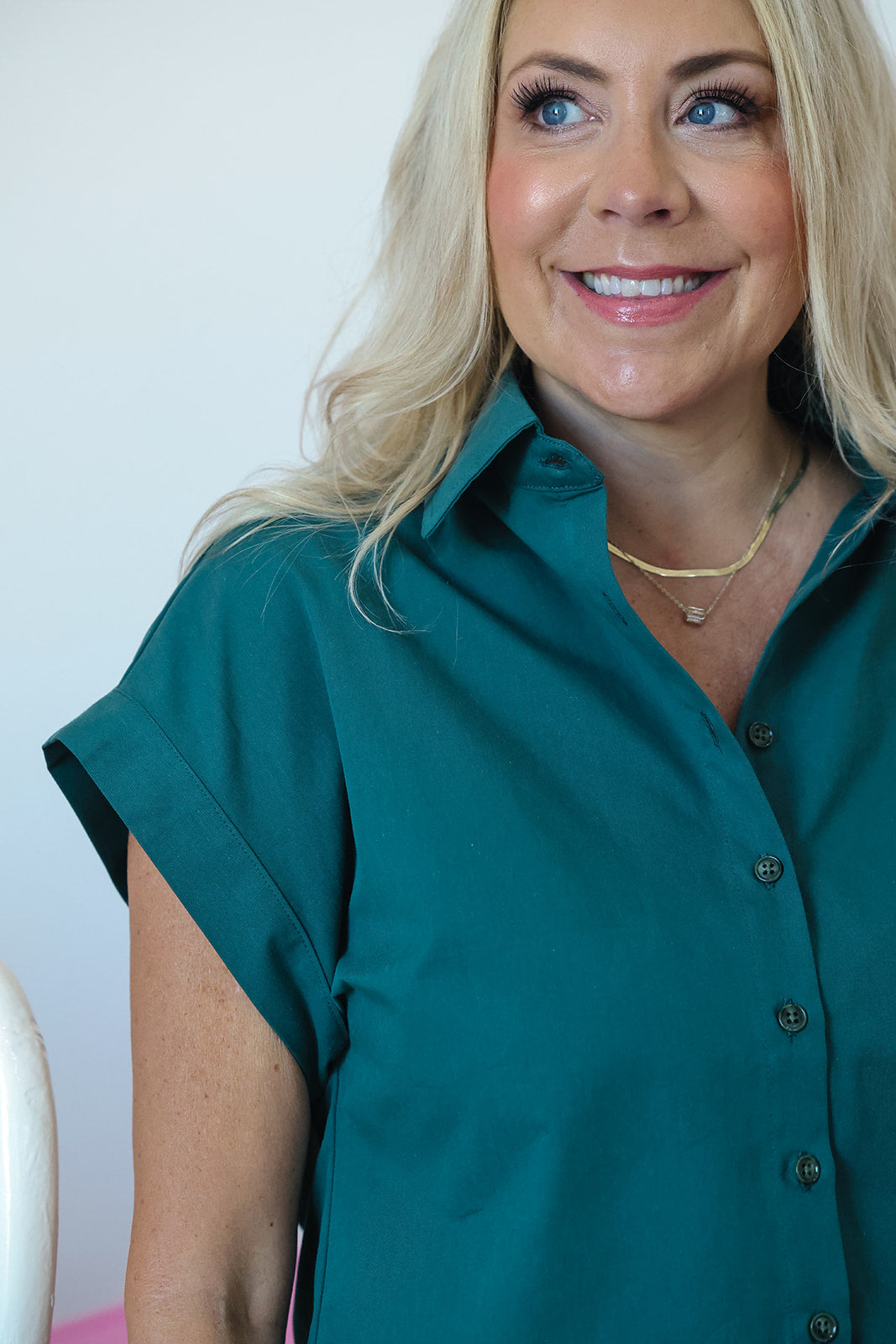 A smiling blonde woman wearing a teal short-sleeve button-up shirt, shown from the chest up against a plain light background.