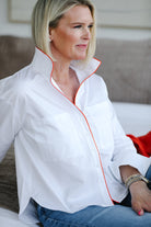 Woman wearing a white blouse with orange piping sitting on a couch.