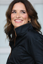 Woman wearing a black blouse with brown piping with a blurred background