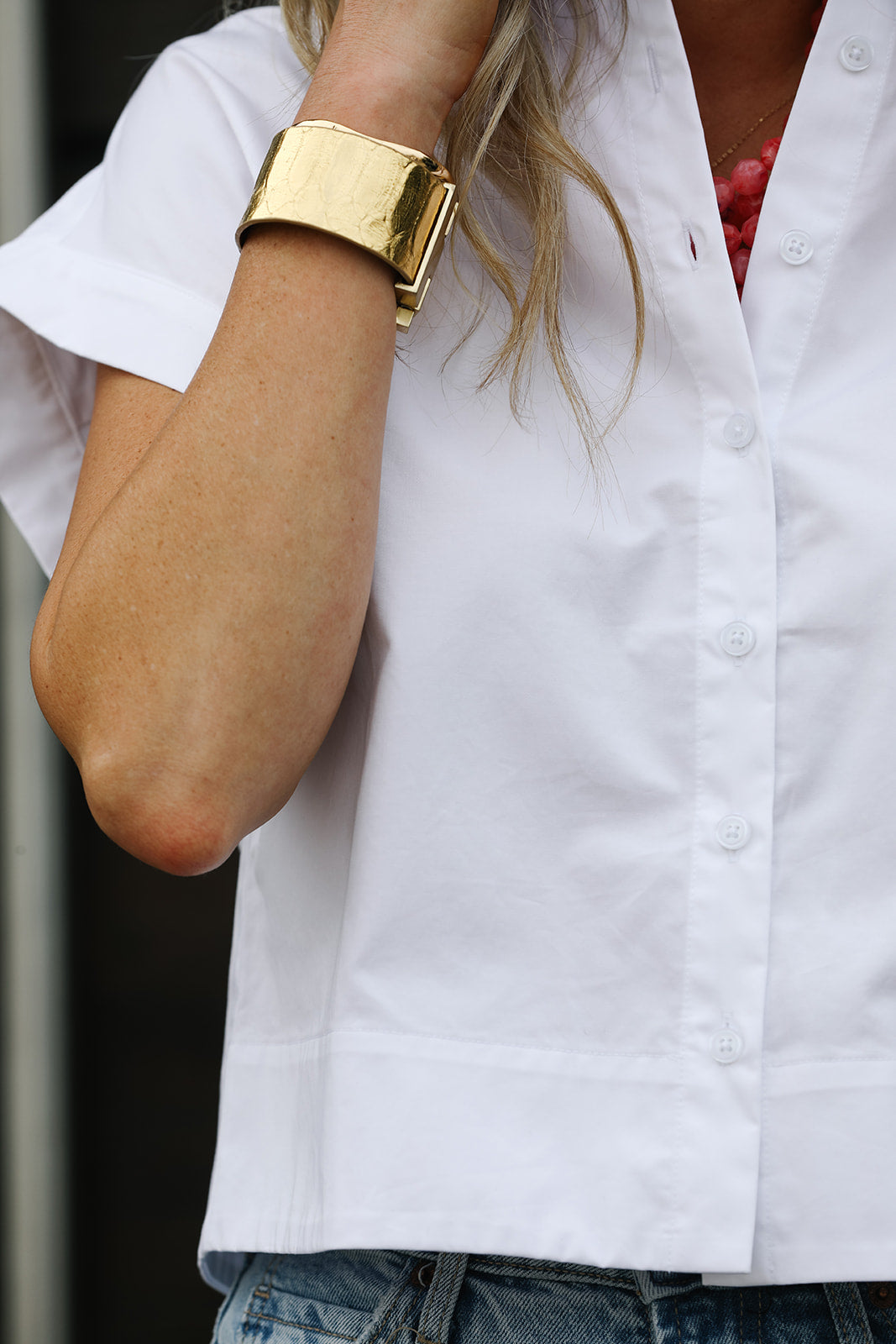 Person wearing a gold bracelet on a white short sleeved crisp shirt with a blurred background