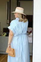 Woman wearing a light blue dress and beige hat, holding a wooden clutch.