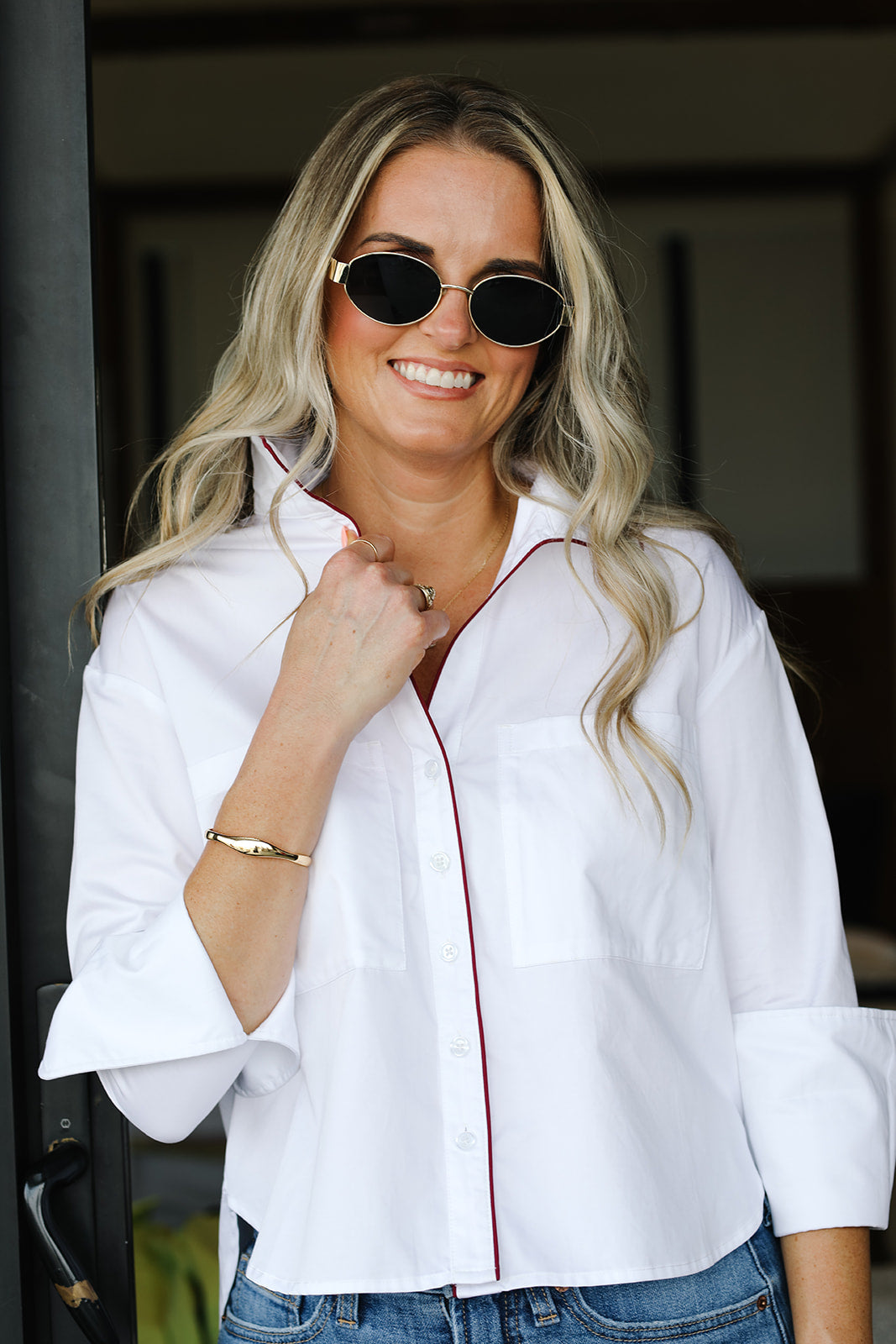 Woman wearing a white blouse with maroon trim and sunglasses, standing indoors.