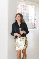 Black, crisp long sleeve shirt with a popped collar, pullover style. Worn with a gold sparkle skirt.