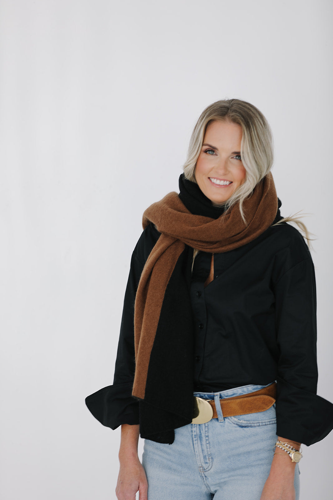 Woman wearing a black sweater, brown scarf, and light blue jeans against a white background