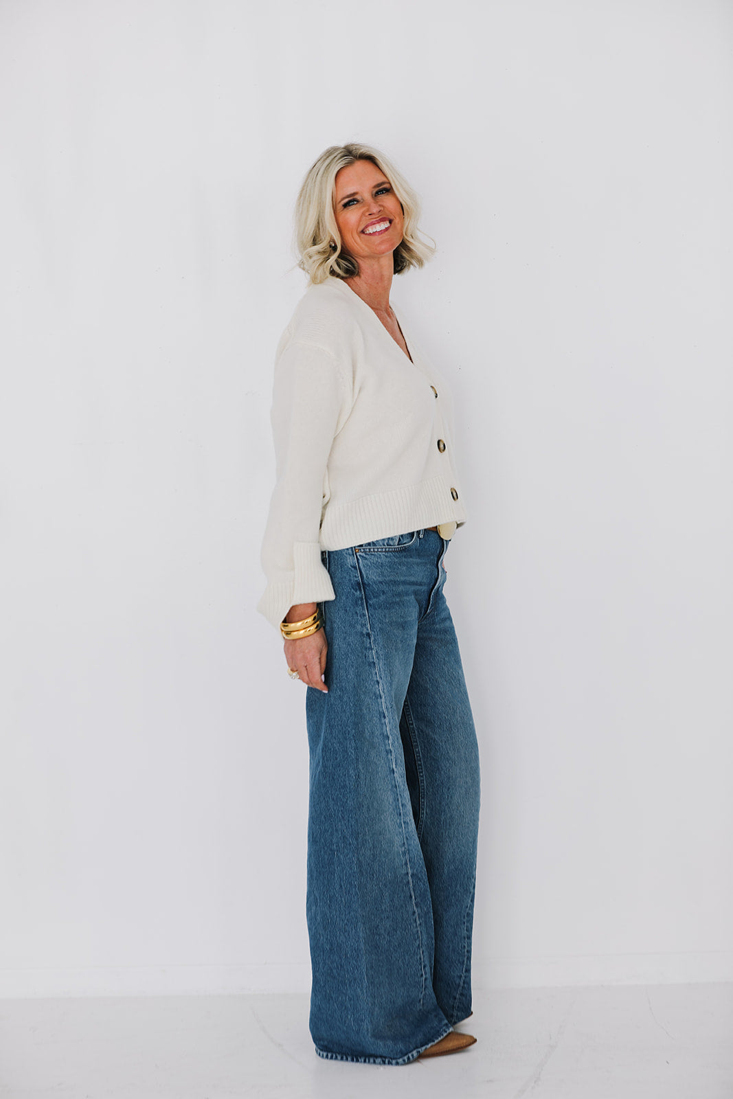 Woman wearing a cream cardigan and blue jeans against a white background