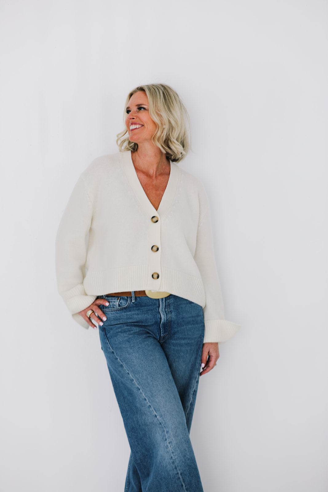 Woman wearing a cream cardigan and blue jeans against a white background