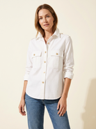 Woman wearing a white shirt with rolled-up sleeves and blue jeans on a beige background